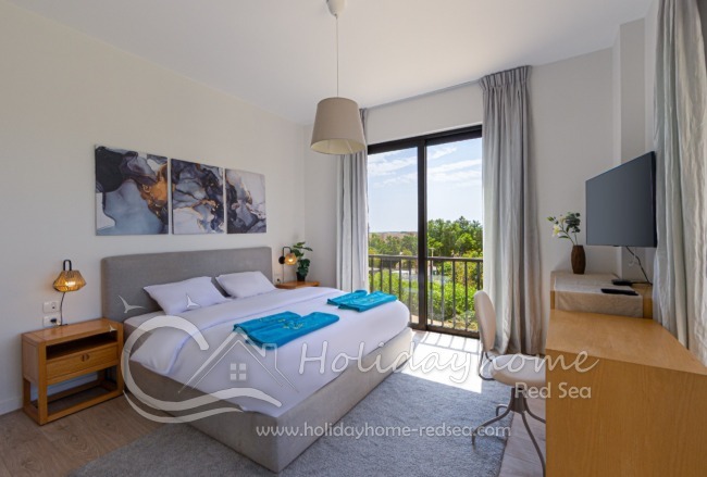 Bedroom 2 with a large double bed, wardrobe, workspace, TV, and access to the balcony